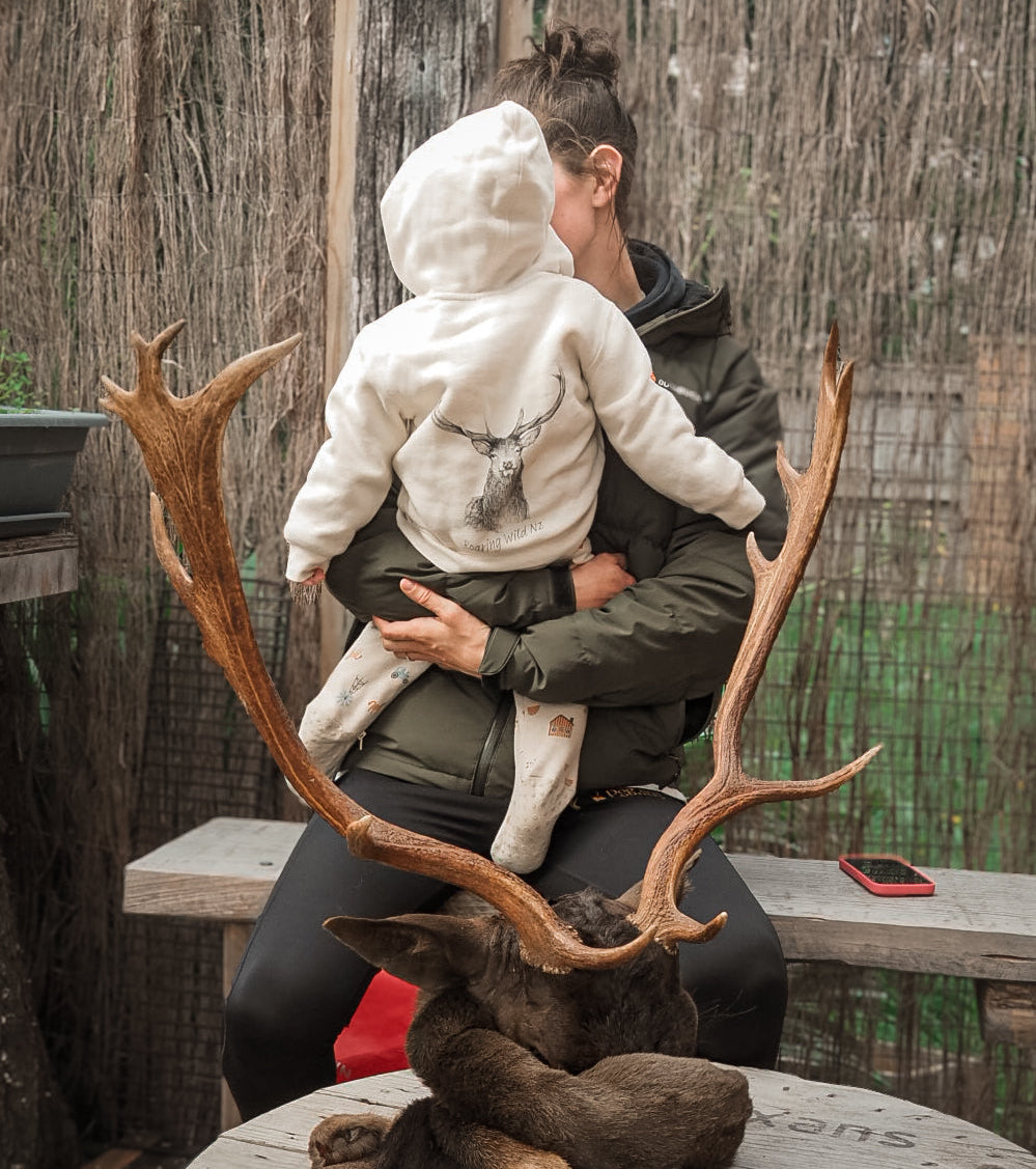 Person holding a child in front of a deer head mount with large antlers.